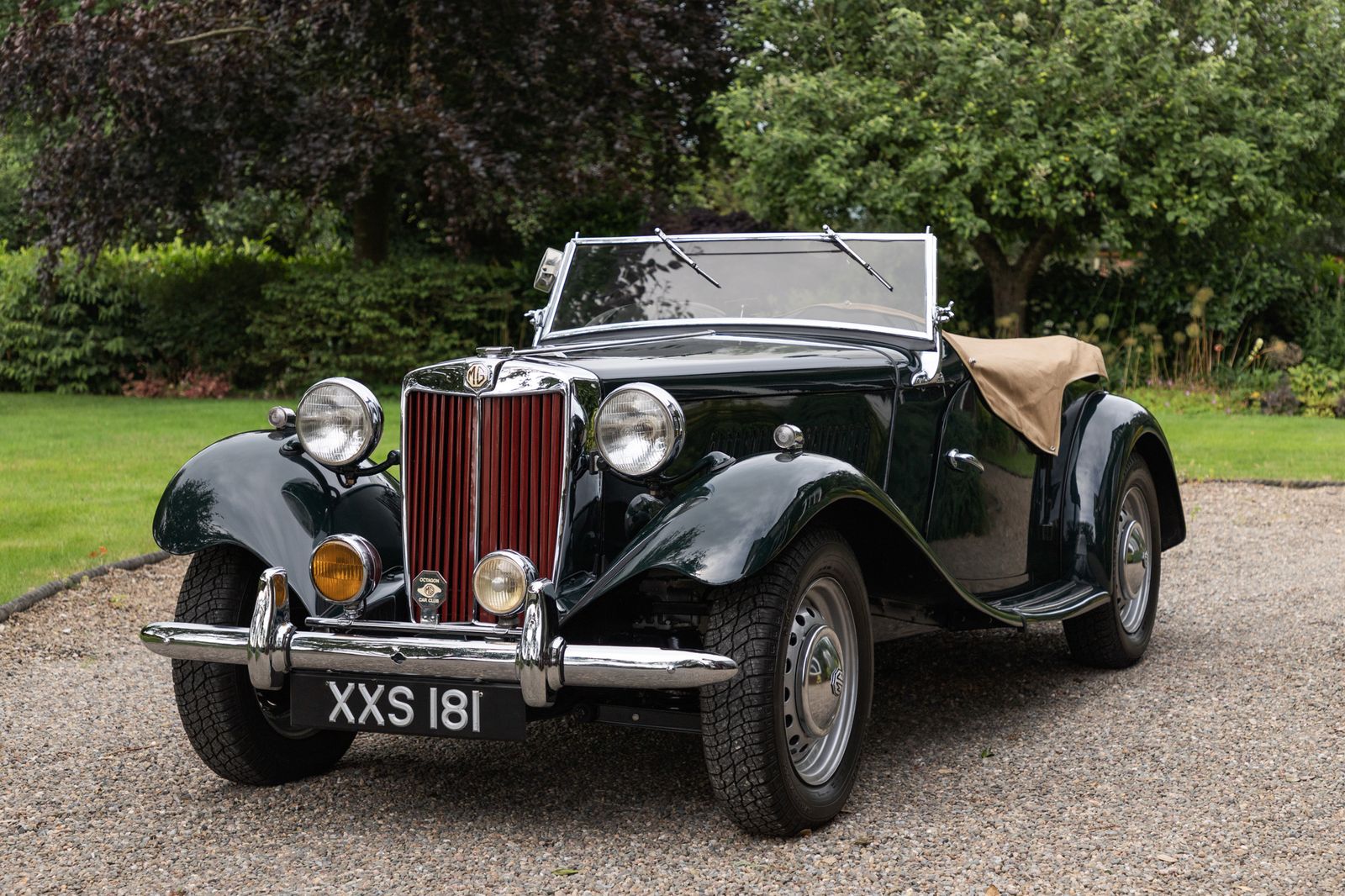 A dark green MG TD classic roadster on a gravel drive with chrome headlamps