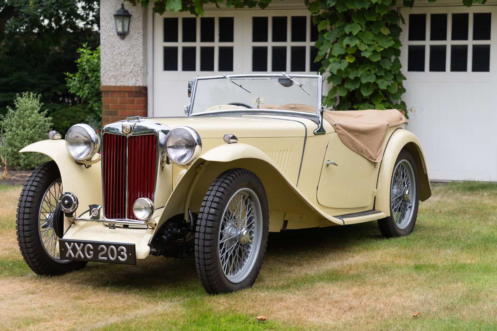 A cream MG TC photographed front three-quarters beside a garage